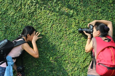 一个女人在拍一个女人倚在绿草墙上的照片